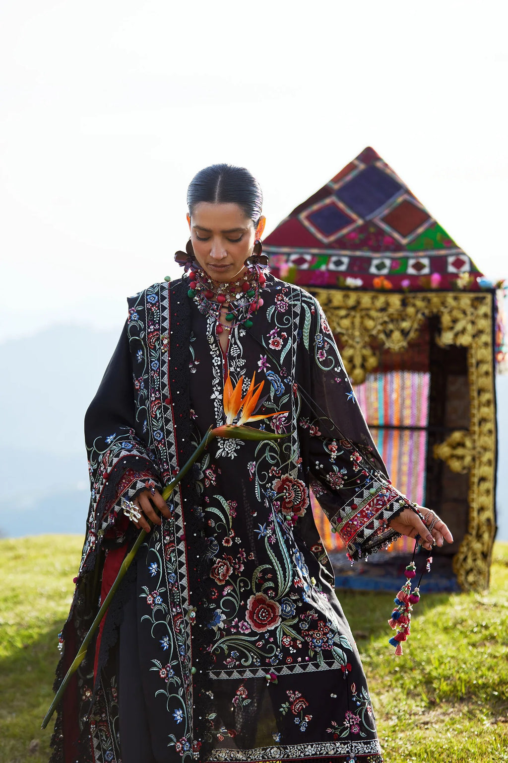 Woman in a patterned dress holding a flower in front of a colorful tent.