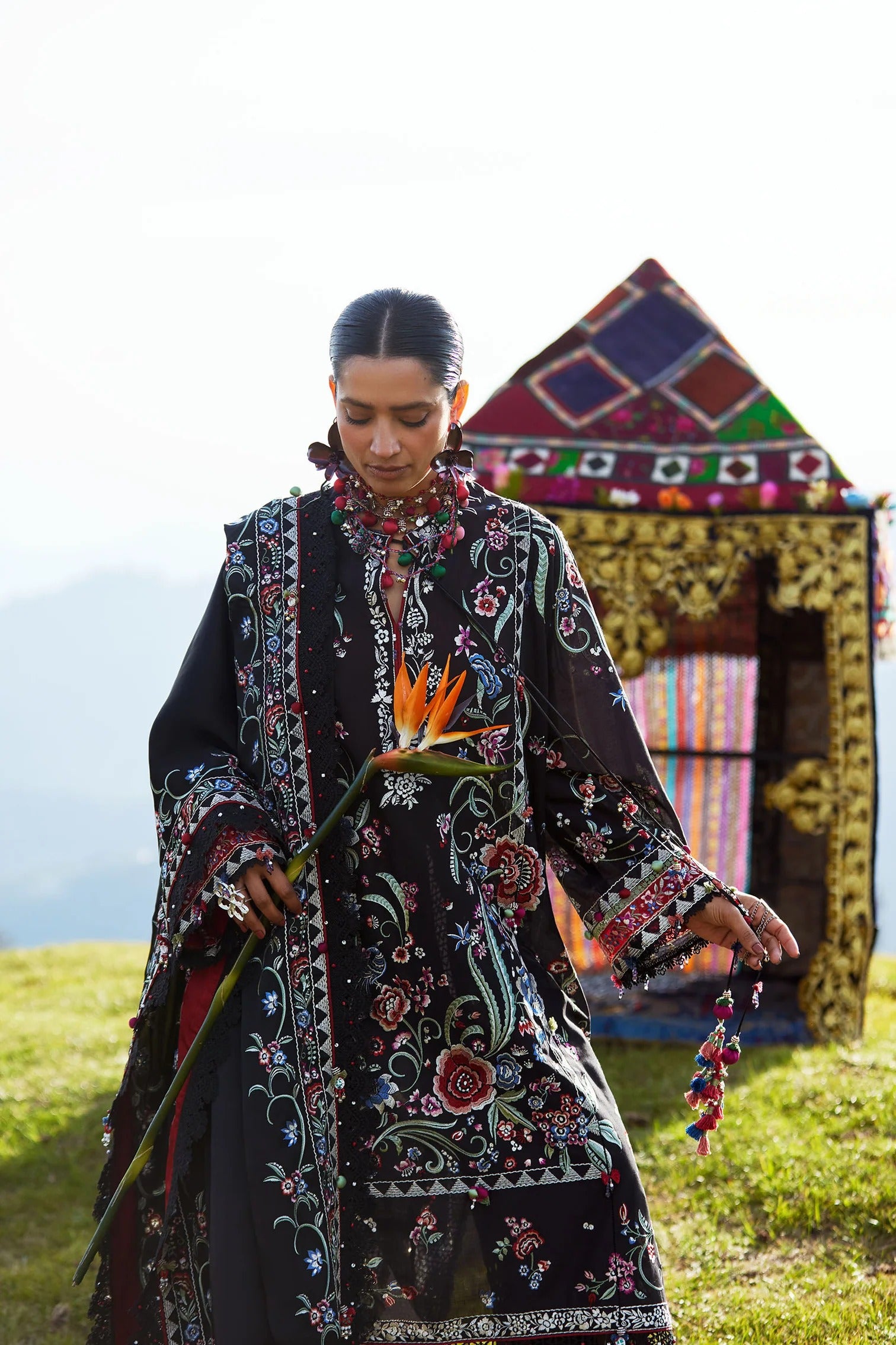 Woman in a patterned dress holding a flower in front of a colorful tent.