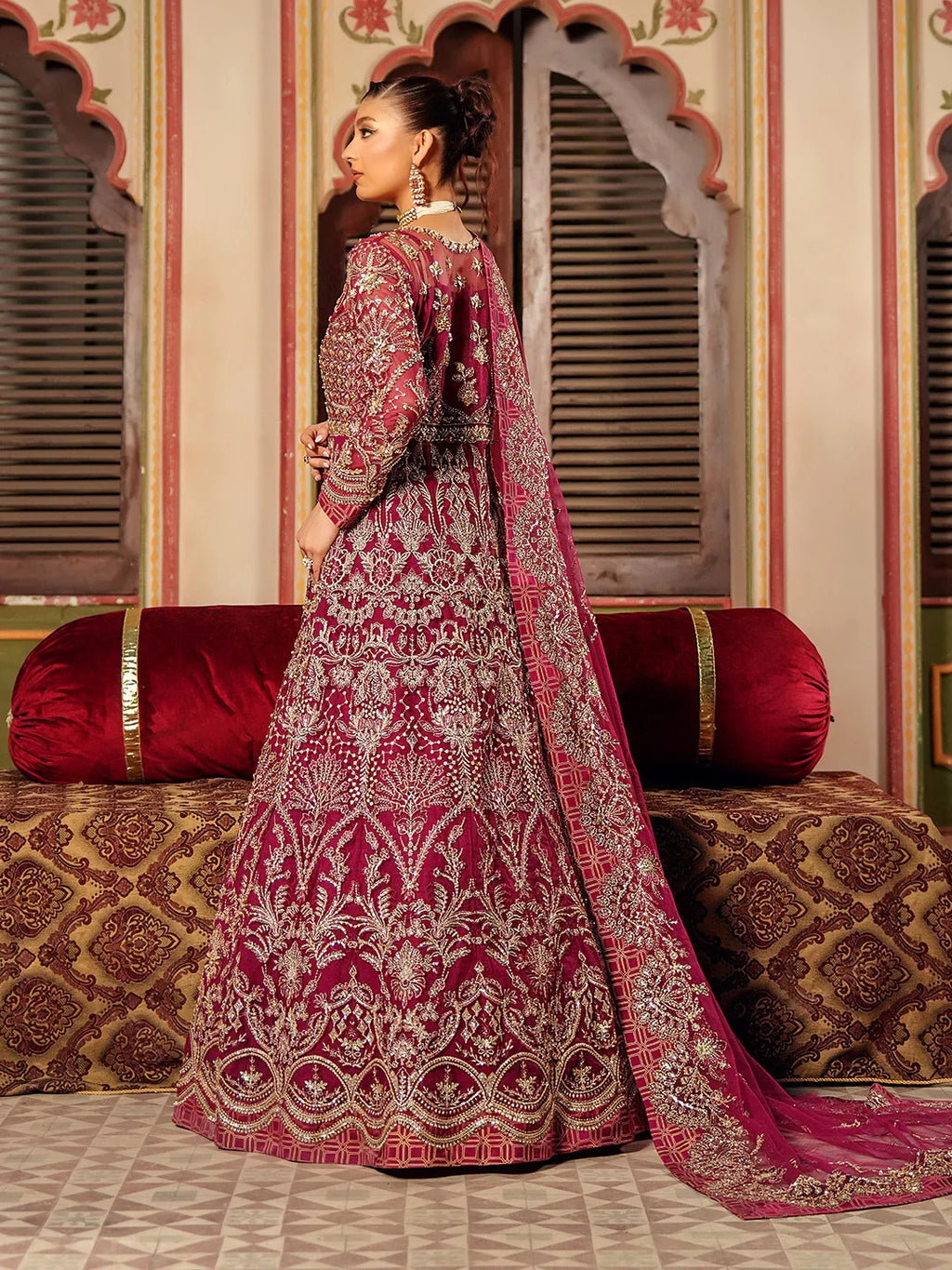 Woman in a traditional embroidered pink and red outfit standing in an ornate room.