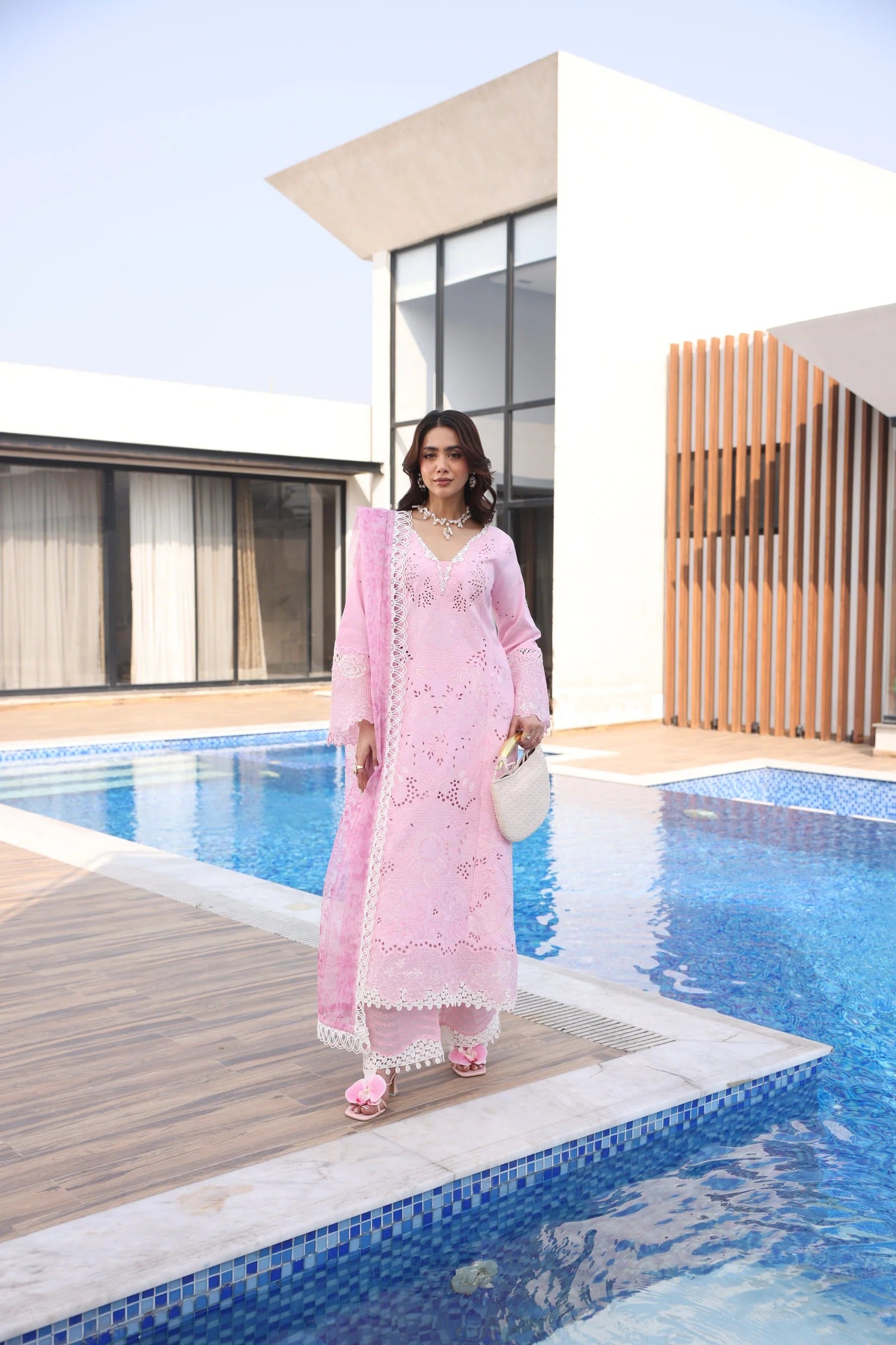 Woman in a pink traditional outfit standing by a pool with modern architecture in the background