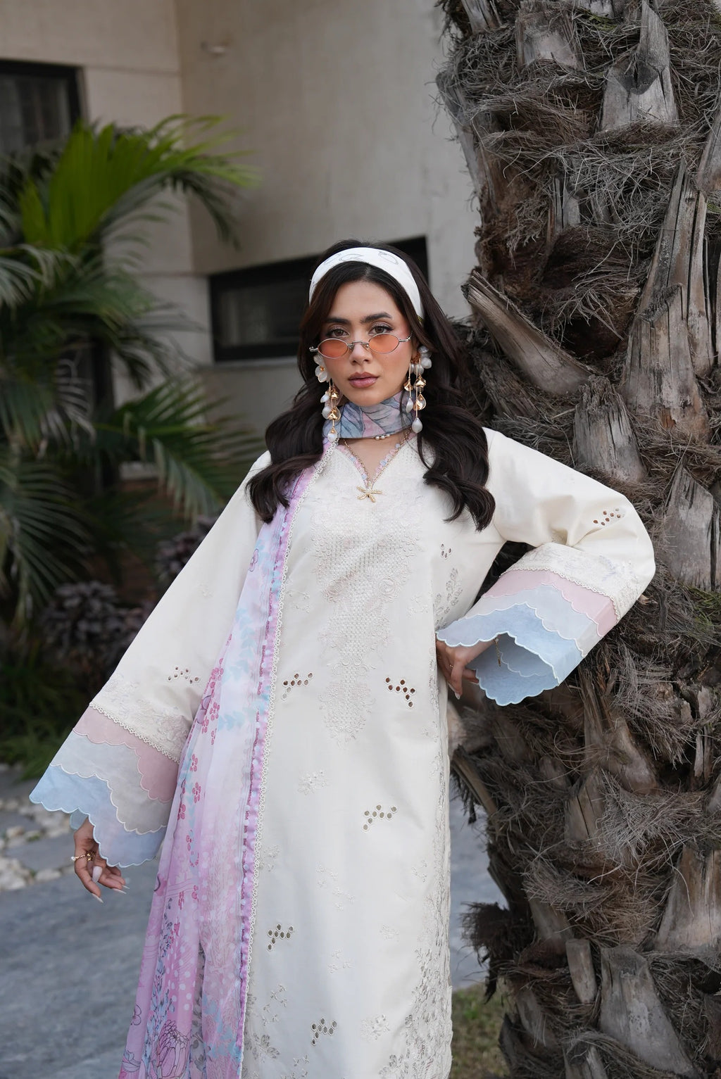 Woman in a white traditional outfit with colorful scarf standing outdoors.