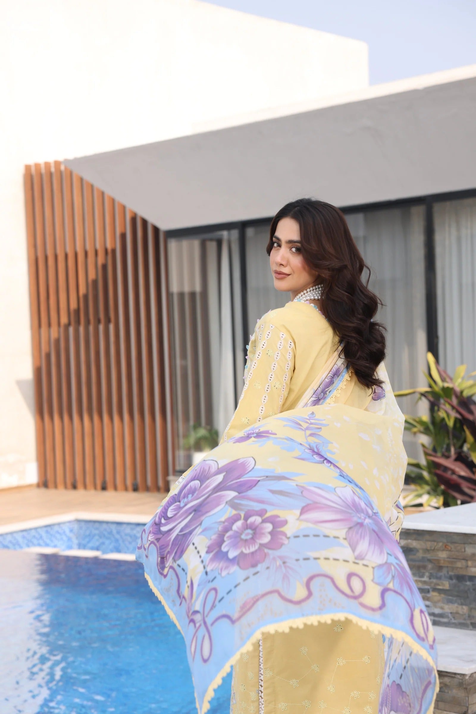 Woman holding a colorful scarf by a poolside with modern architecture in the background