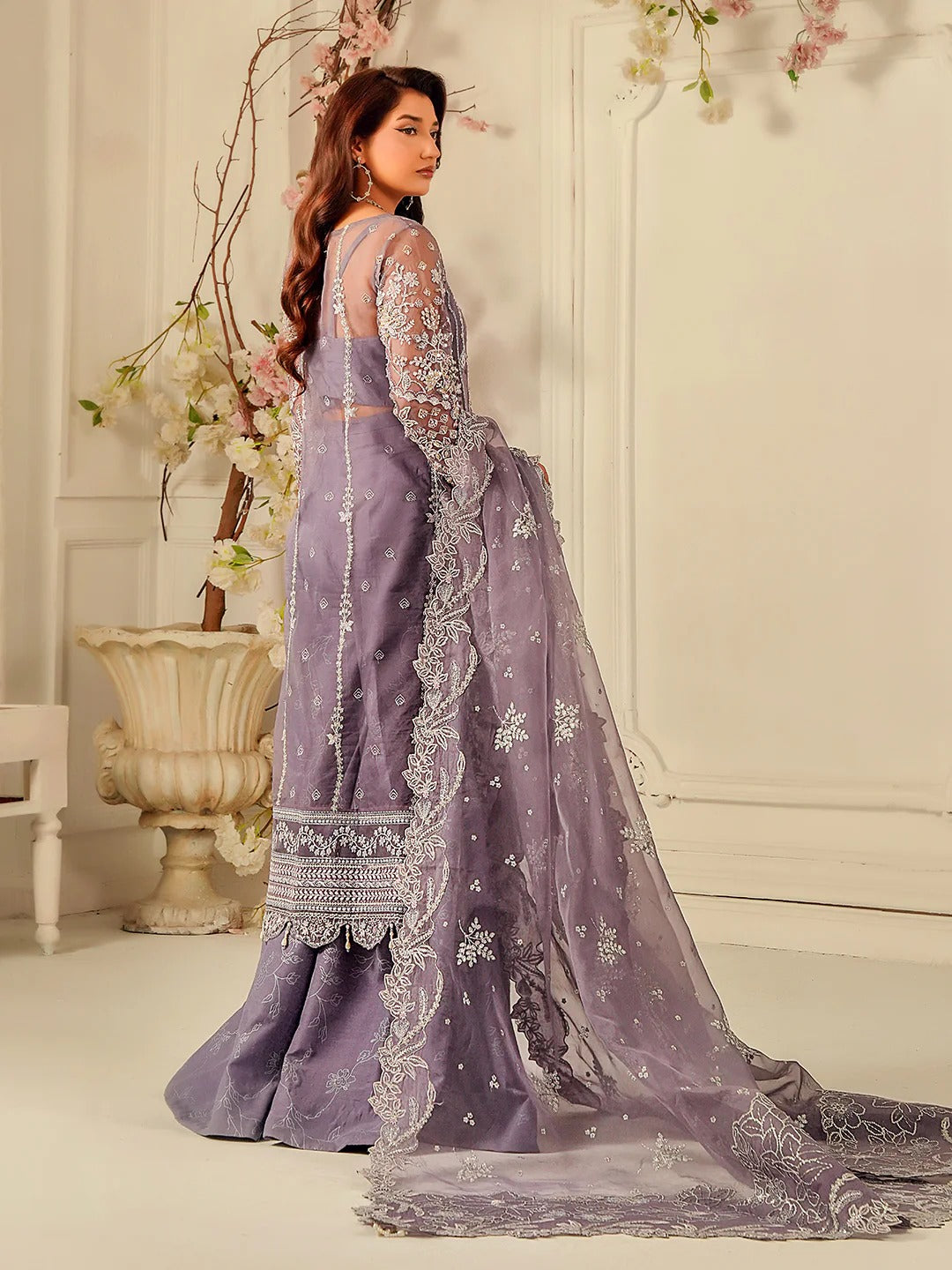 Woman in a lavender saree with intricate embroidery in a decorated room.