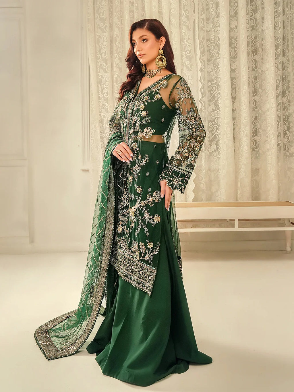 Woman wearing a green embroidered traditional outfit with a matching dupatta in a neutral setting.