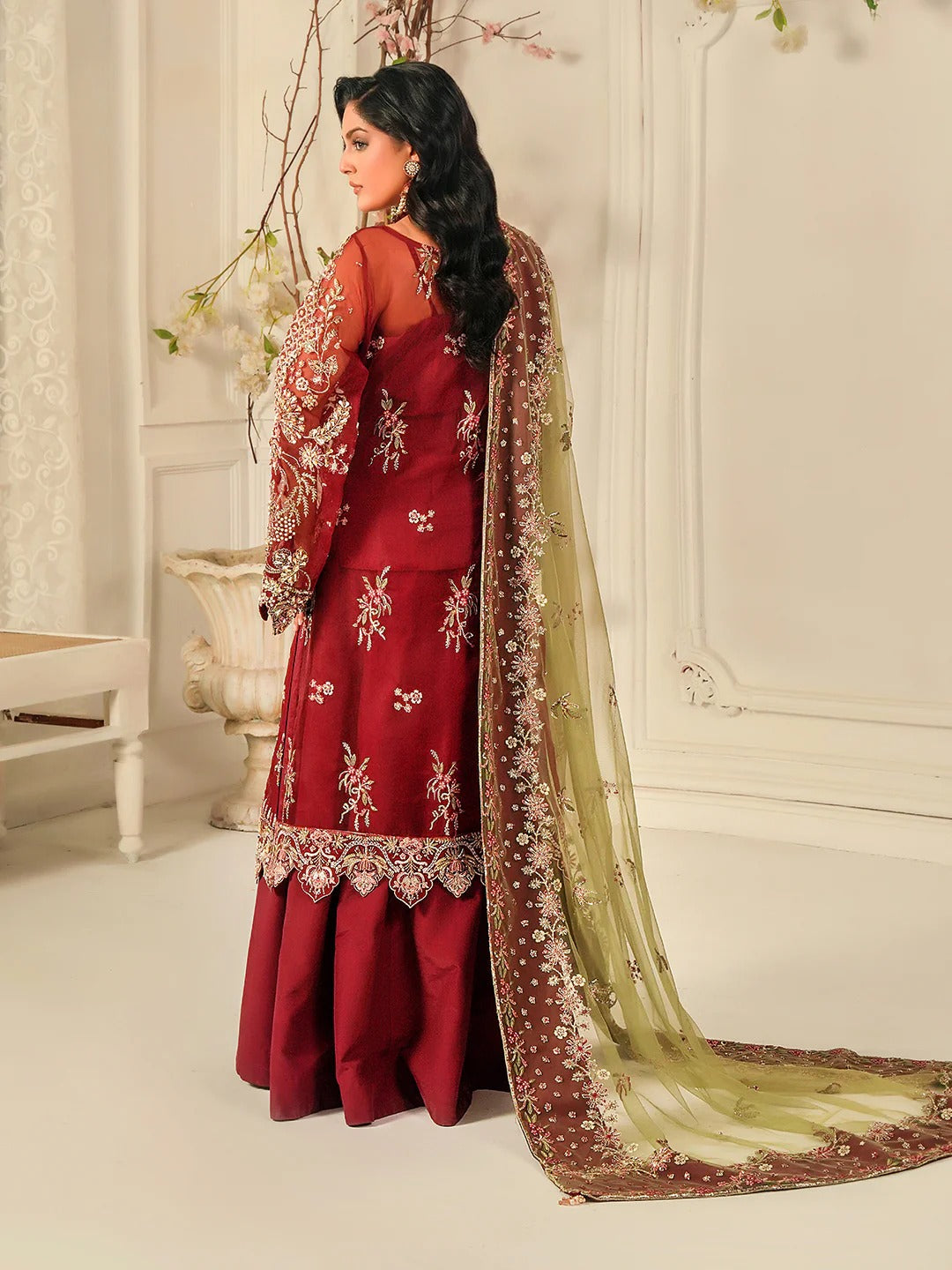 Woman in a red embroidered outfit with a matching dupatta in a decorative setting