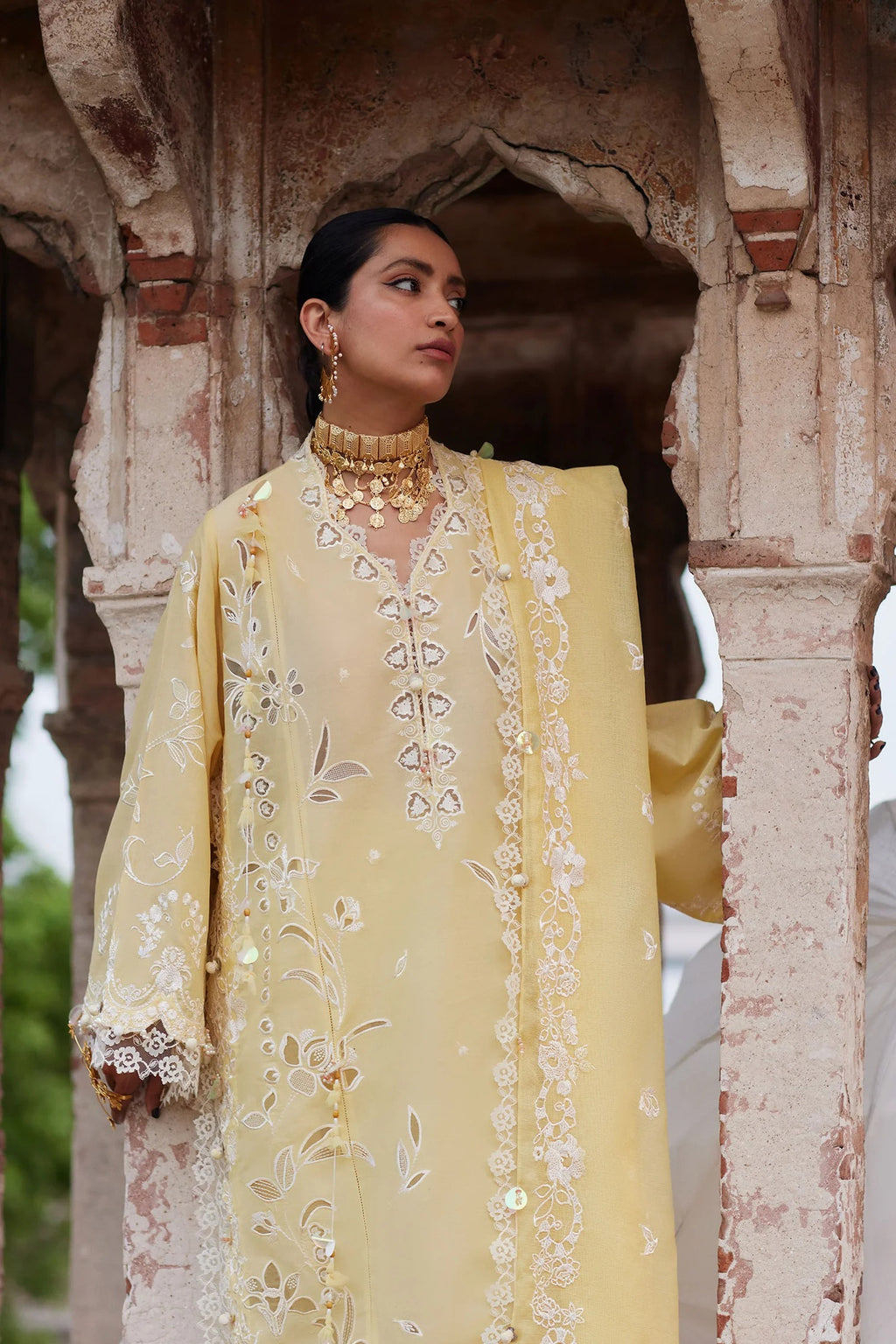 Woman in a yellow embroidered outfit standing under an archway.