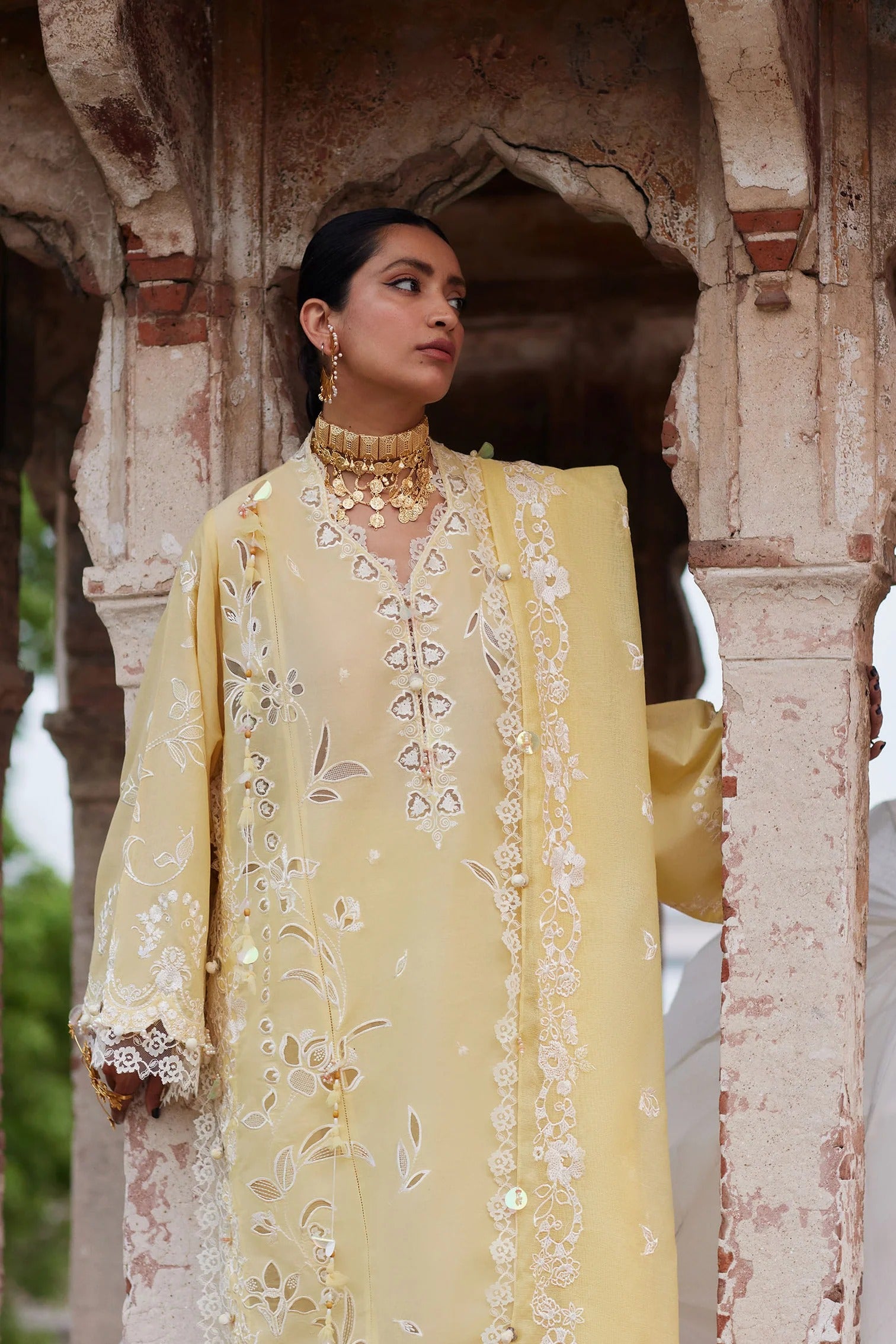 Woman in a yellow embroidered outfit standing under an archway.