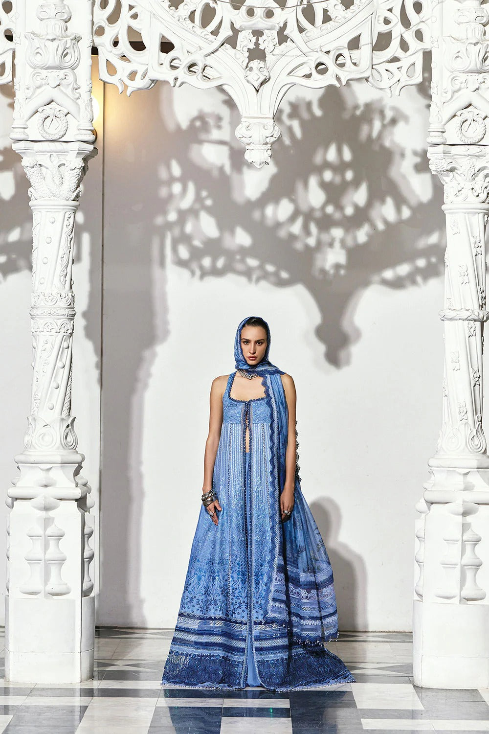 Woman in a blue dress standing in front of decorative white columns with intricate patterns.