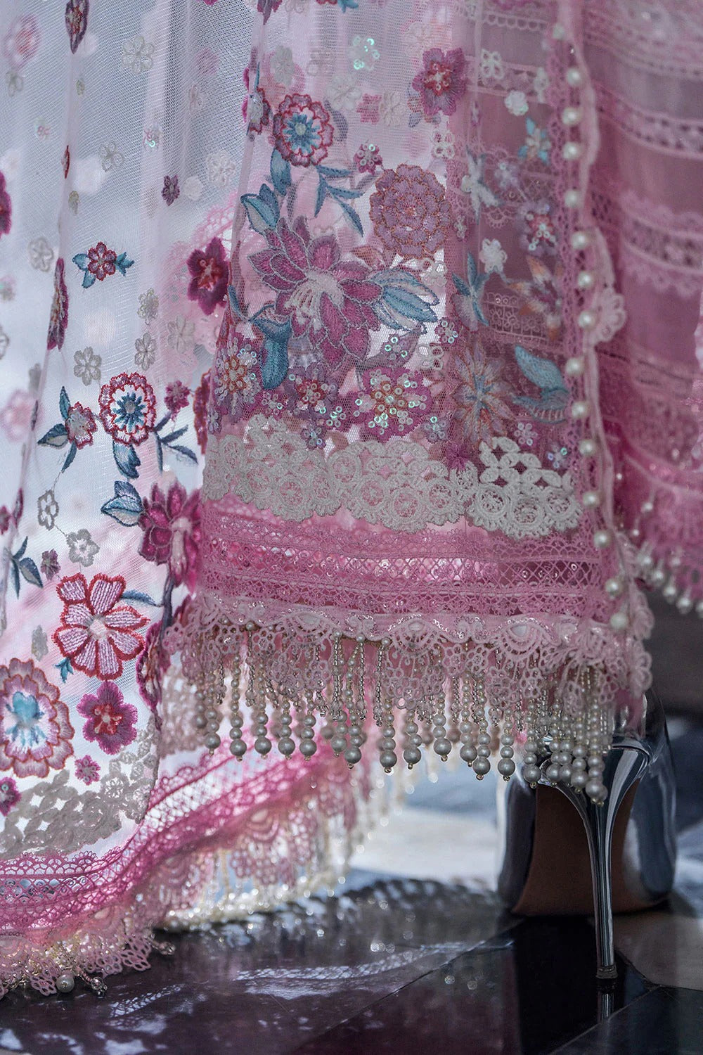 Close-up of a pink embroidered garment with floral patterns and fringe details.