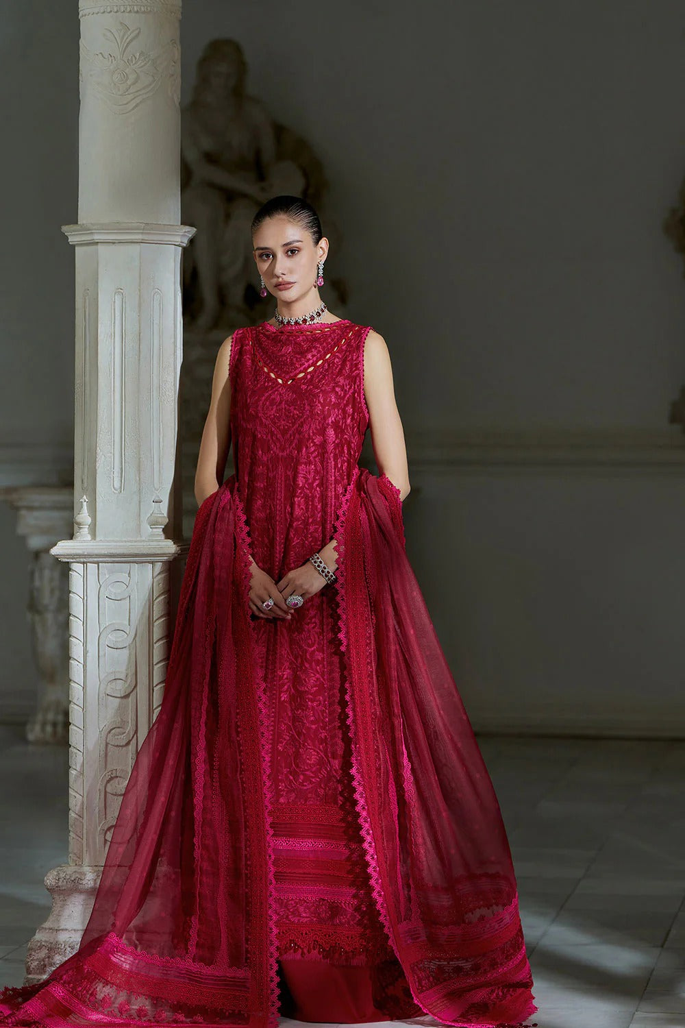 Woman in a red embroidered dress standing in an elegant indoor setting.