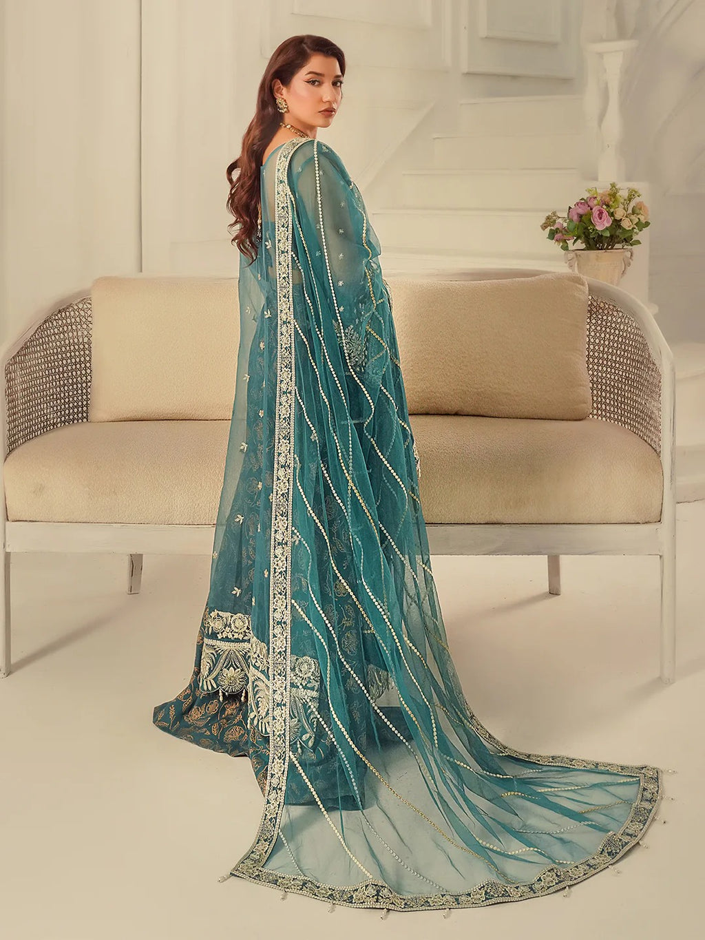 Woman wearing a teal embroidered saree in a modern interior setting