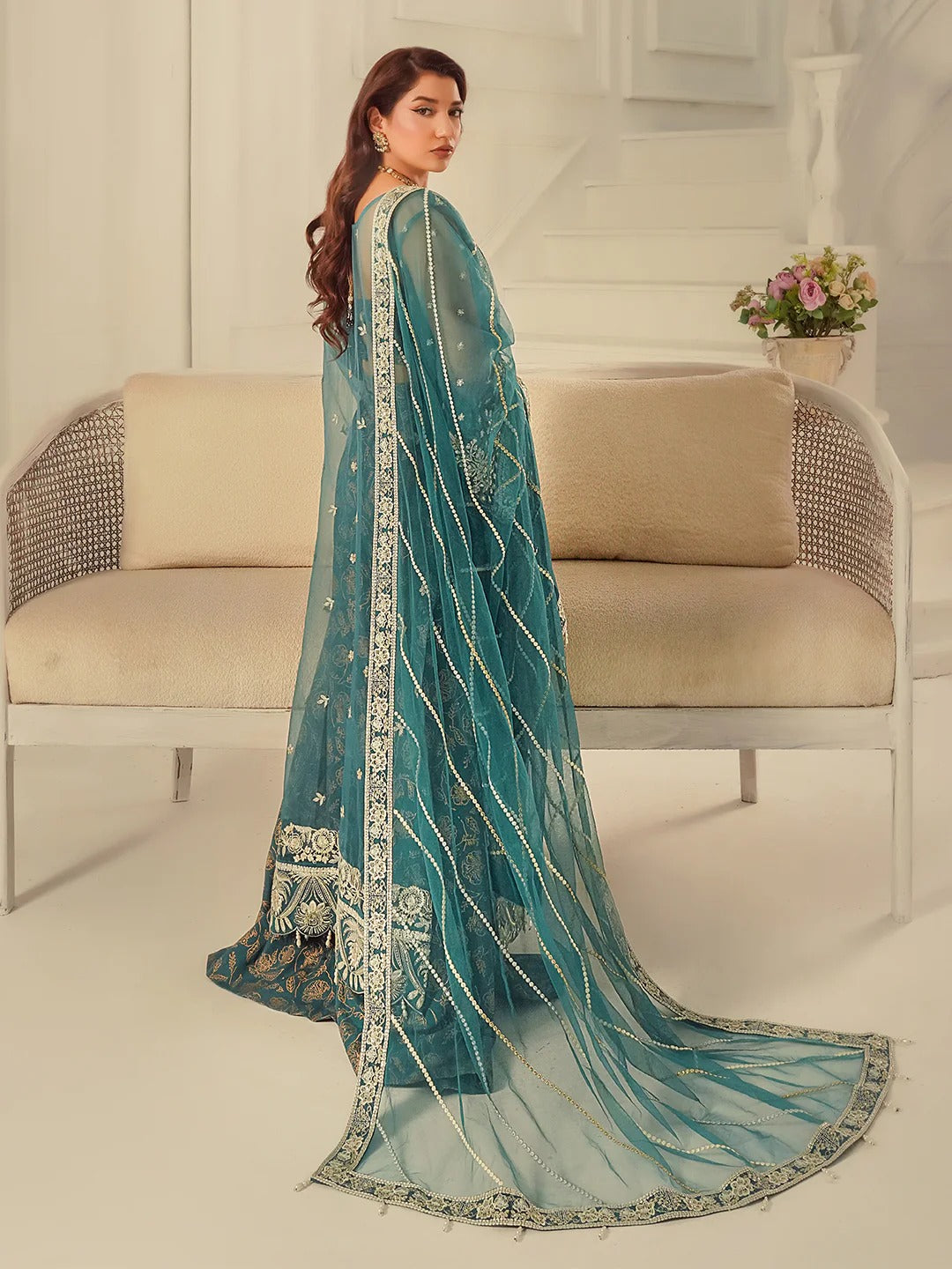 Woman wearing a teal embroidered saree in a modern interior setting