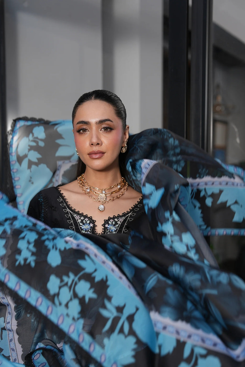 Woman wearing a black and blue patterned garment with jewelry indoors.