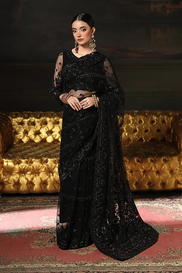 Woman in a black saree with gold details against a dark background