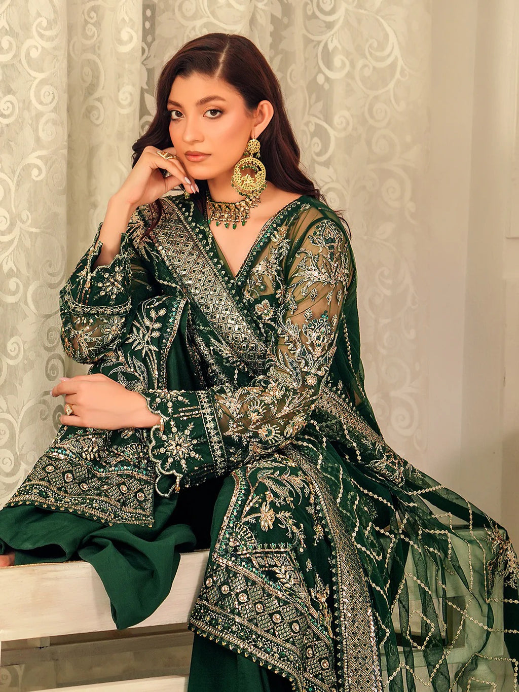 Woman wearing a green embroidered traditional outfit with gold detailing against a neutral background