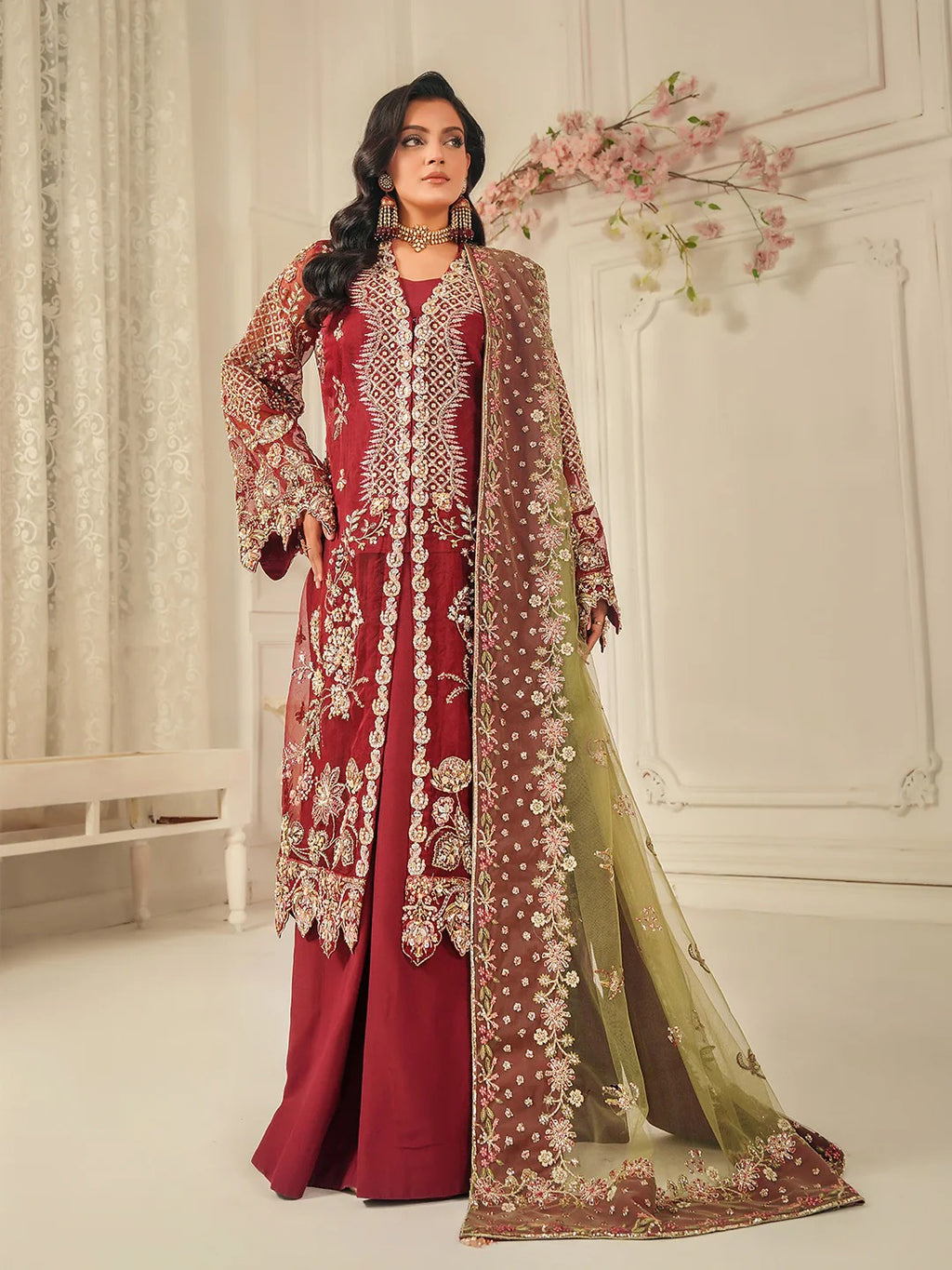 Woman wearing a red embroidered outfit with a matching dupatta in a decorated room.