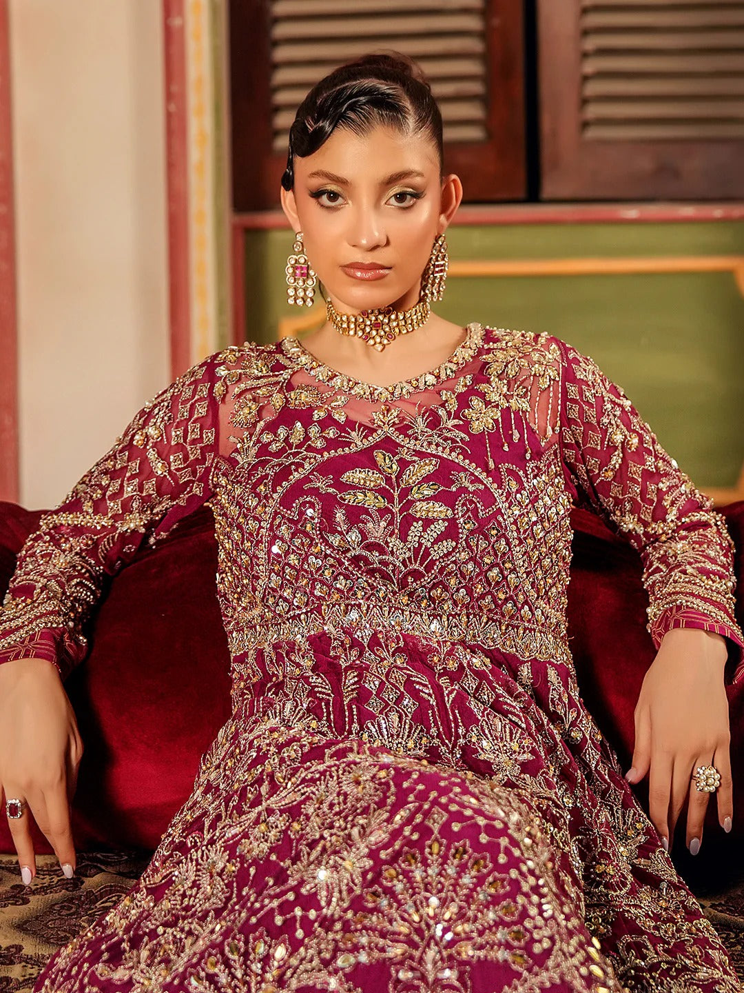Woman in a traditional embroidered dress sitting on a red couch.