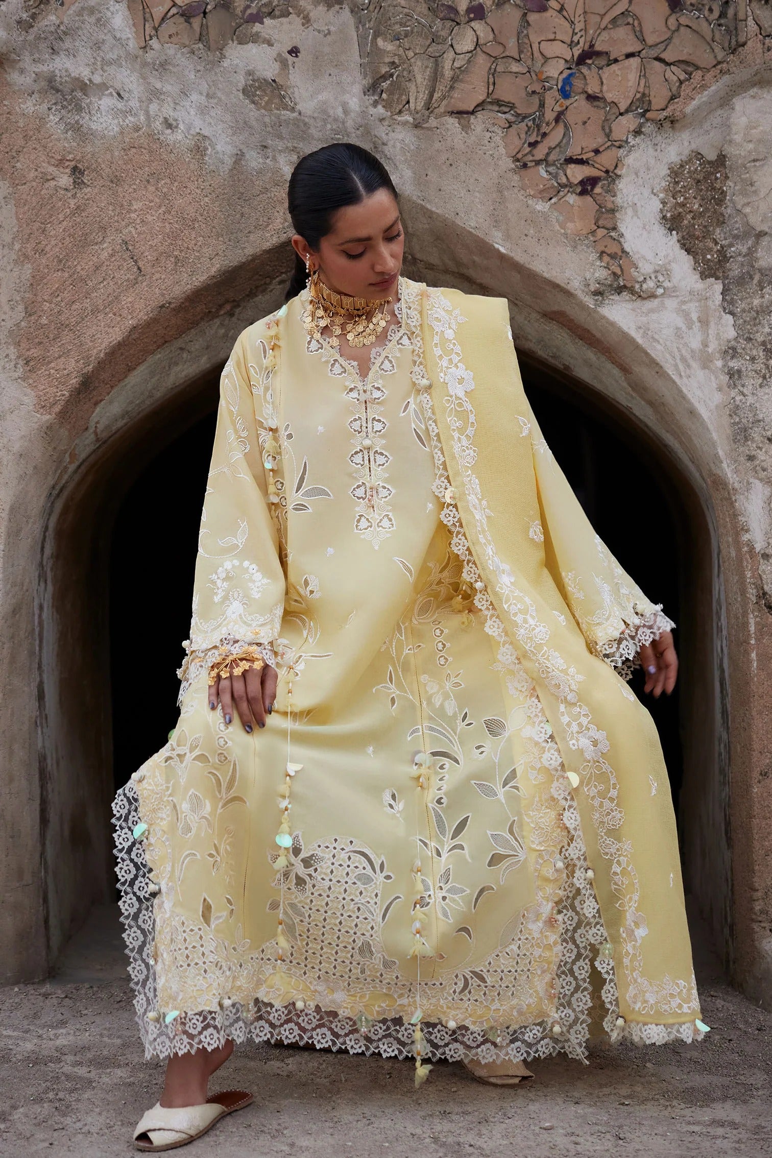 Woman in a yellow embroidered traditional outfit standing in front of an archway.