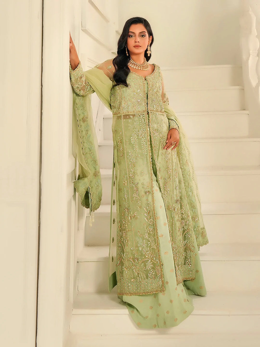 Woman in a light green embroidered traditional outfit standing on a staircase.