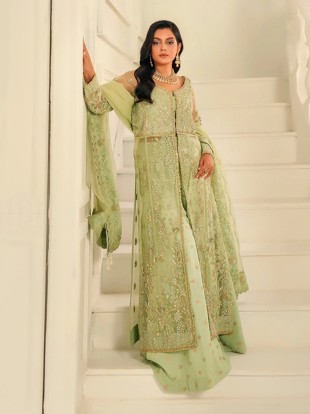 Woman in a light green embroidered traditional outfit standing on a staircase.
