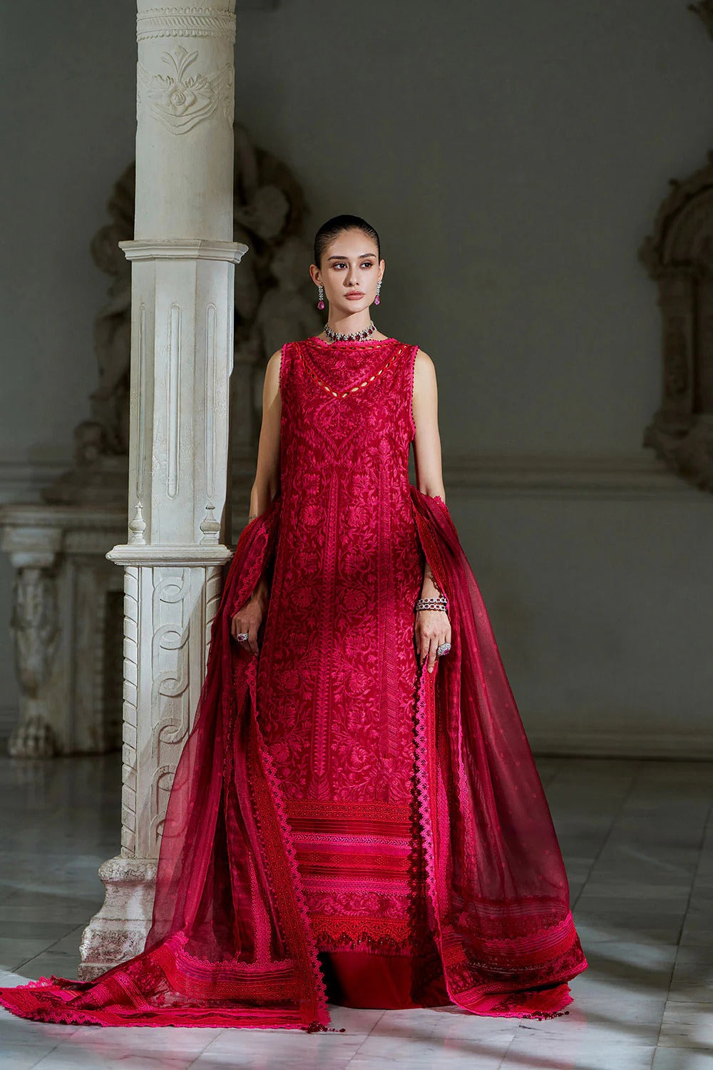 Woman in a red embroidered dress standing in an elegant interior setting.