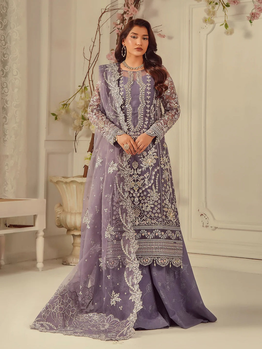 Woman wearing a purple embroidered traditional outfit in an elegant room.