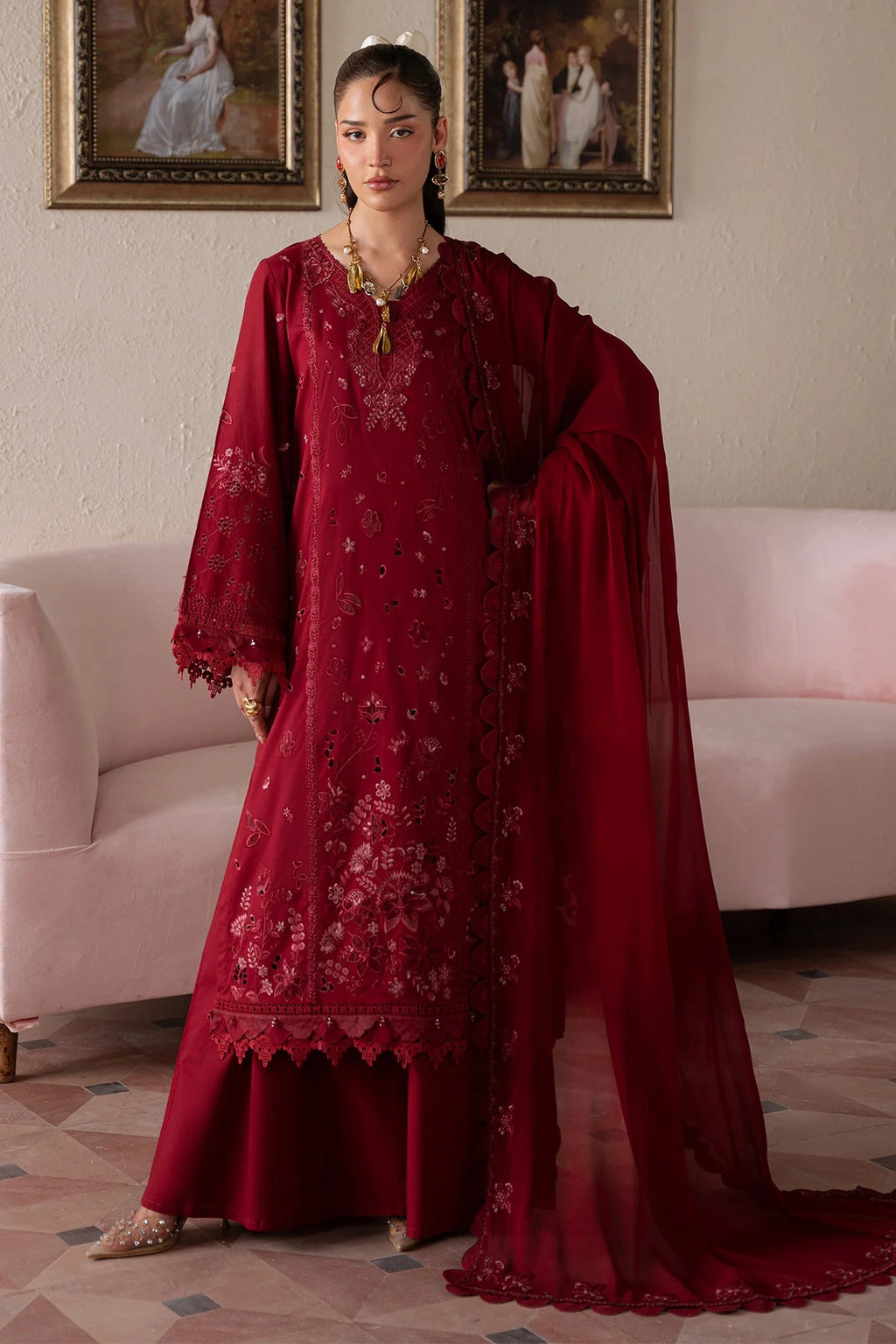 Woman in a red embroidered traditional outfit standing in a room with framed pictures on the wall.
