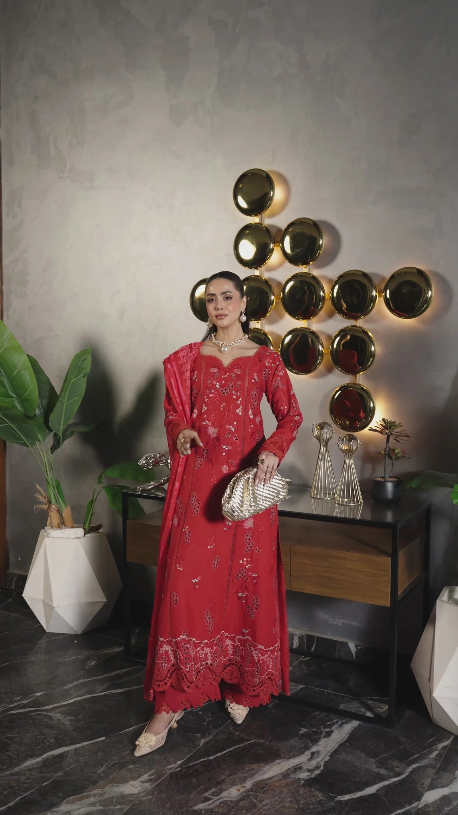 Woman in a red dress standing in a stylish interior setting with decorative wall art.