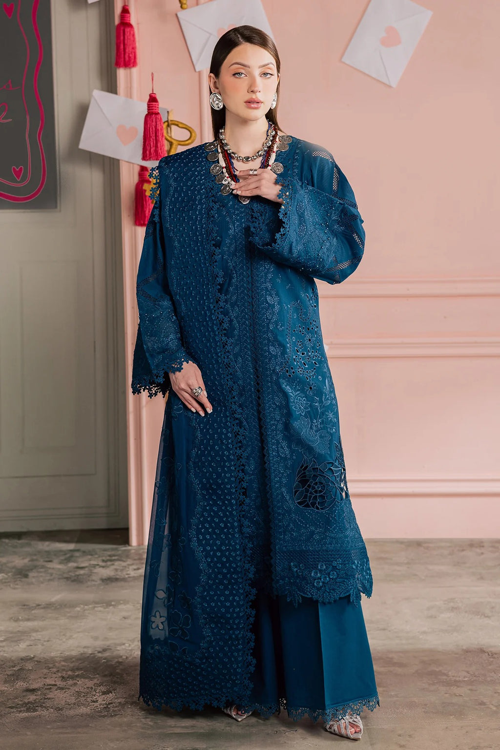 Woman wearing a blue embroidered outfit in an indoor setting with pink walls.