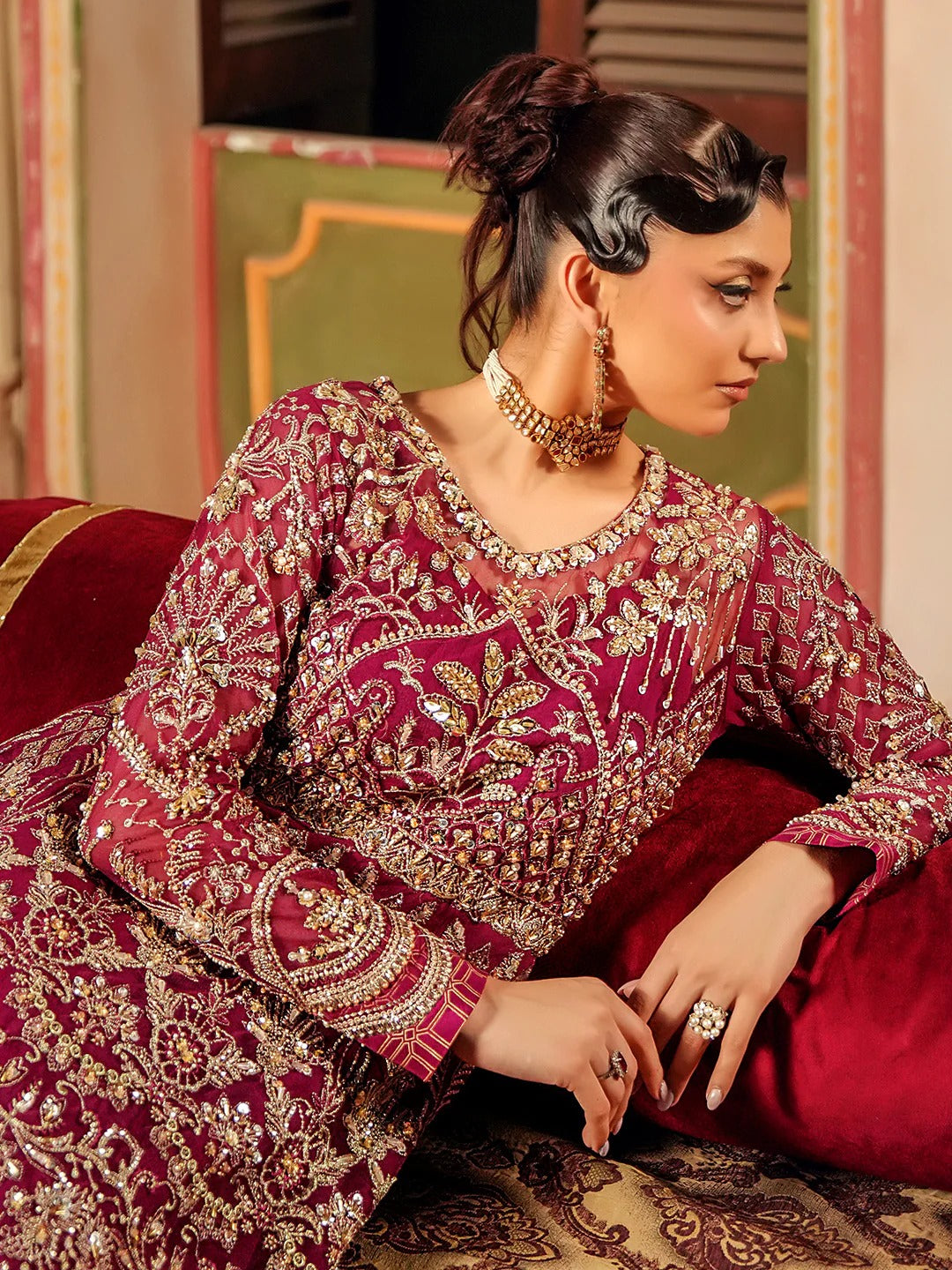 Woman in a traditional embroidered outfit sitting on a red couch.