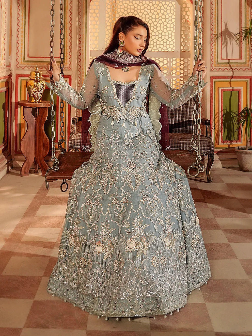 Woman in an ornate embroidered dress standing in a decorated room.