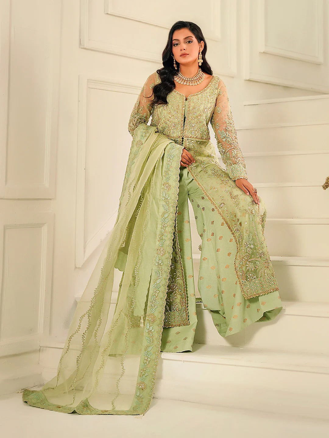 Woman in a light green traditional outfit with intricate patterns on a white staircase.