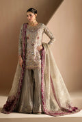 A woman models a traditional South Asian ensemble featuring a heavily embroidered light beige and silver kurta, pleated gray trousers, and a sheer beige dupatta with a deep magenta border.
