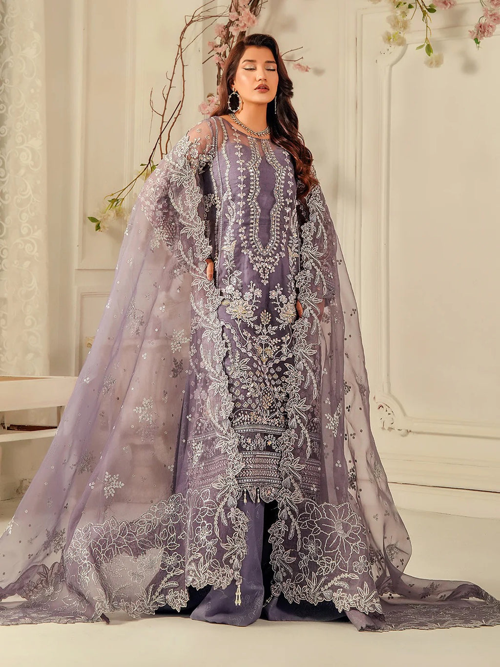 Woman in a purple embroidered outfit with a sheer dupatta in a decorated indoor setting