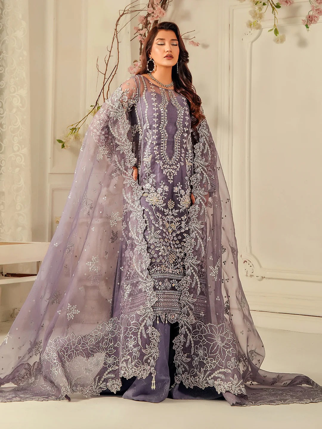 Woman in a purple embroidered outfit with a sheer dupatta in a decorated indoor setting