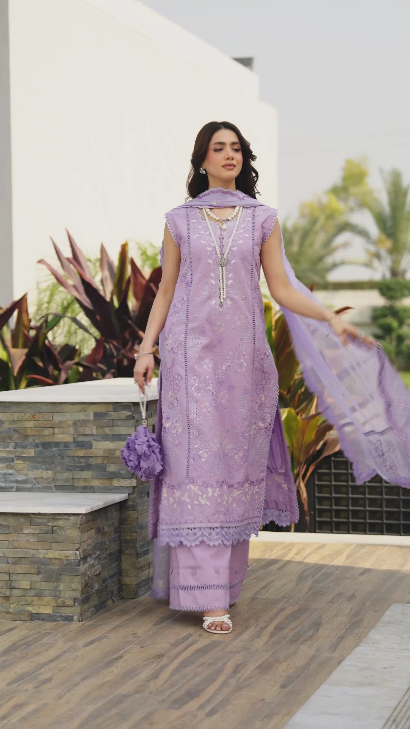 Woman in a purple traditional outfit standing outdoors with plants in the background