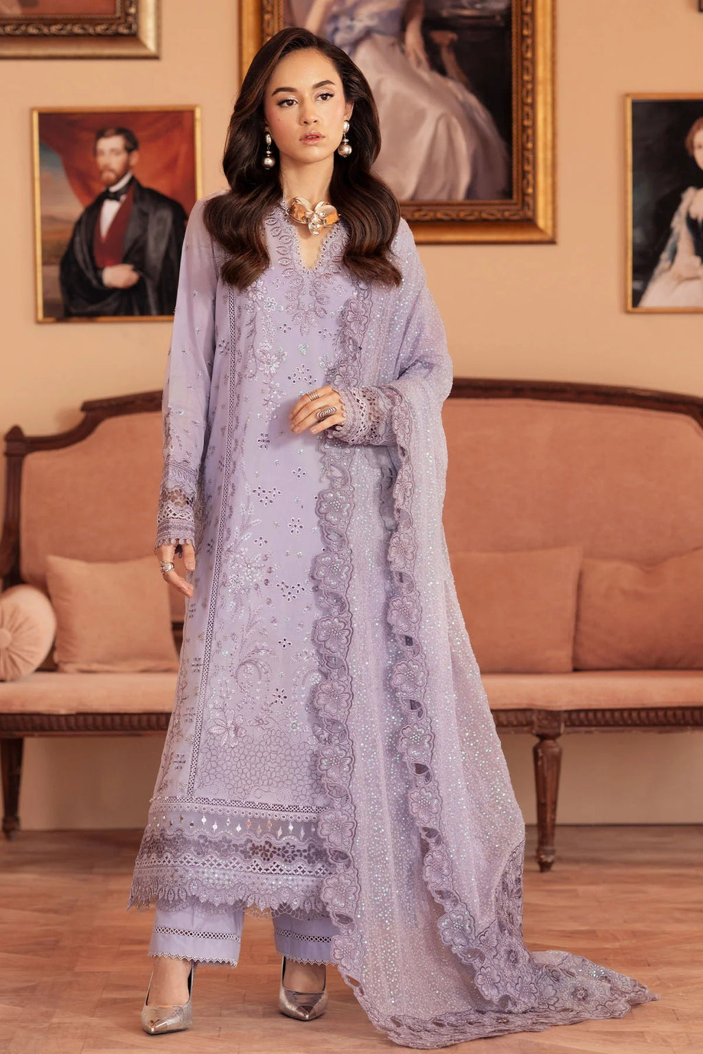 Woman in a light purple embroidered outfit standing in a room with classical decor.