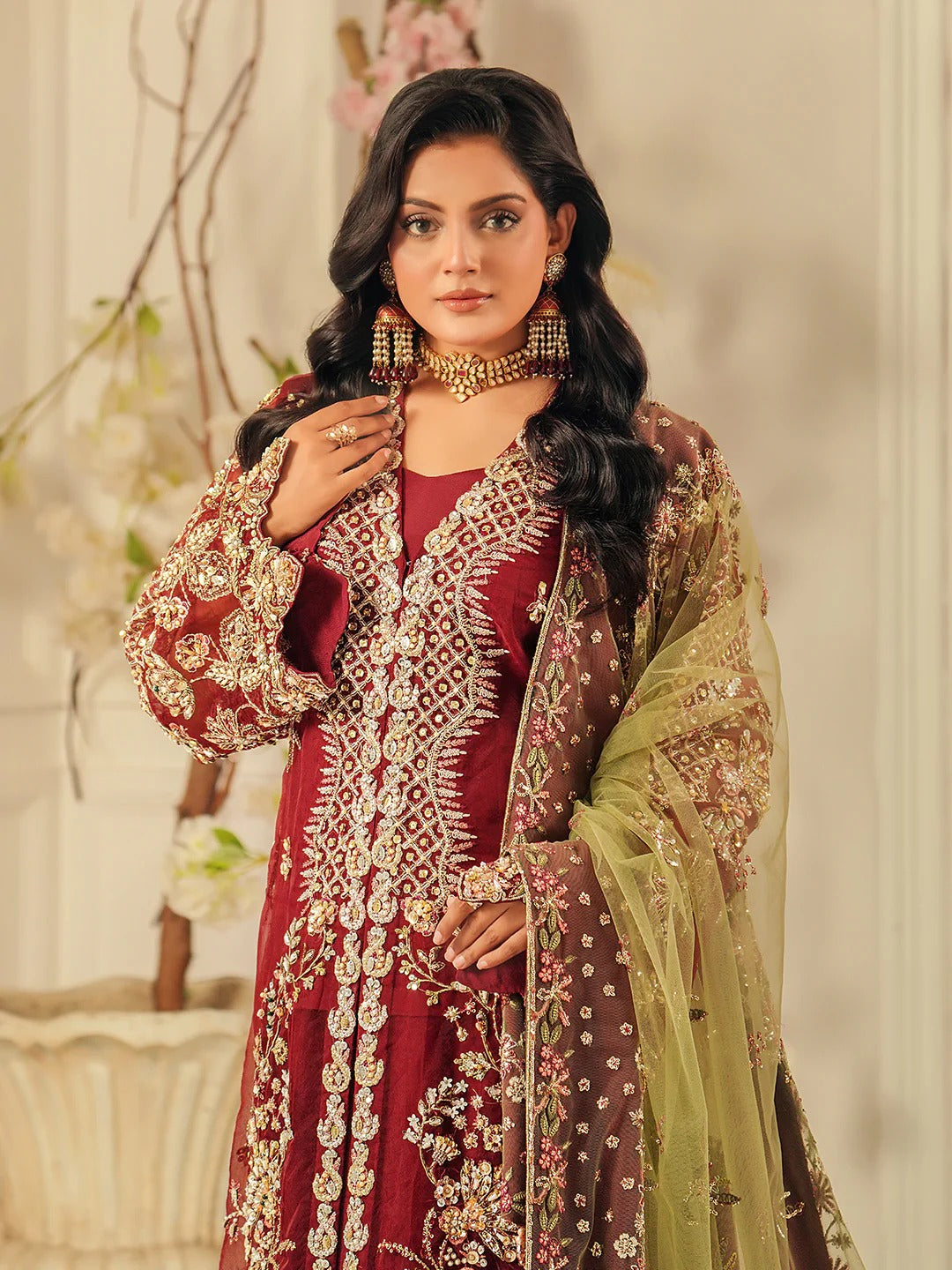Woman in traditional maroon and gold embroidered outfit with green dupatta against a neutral background
