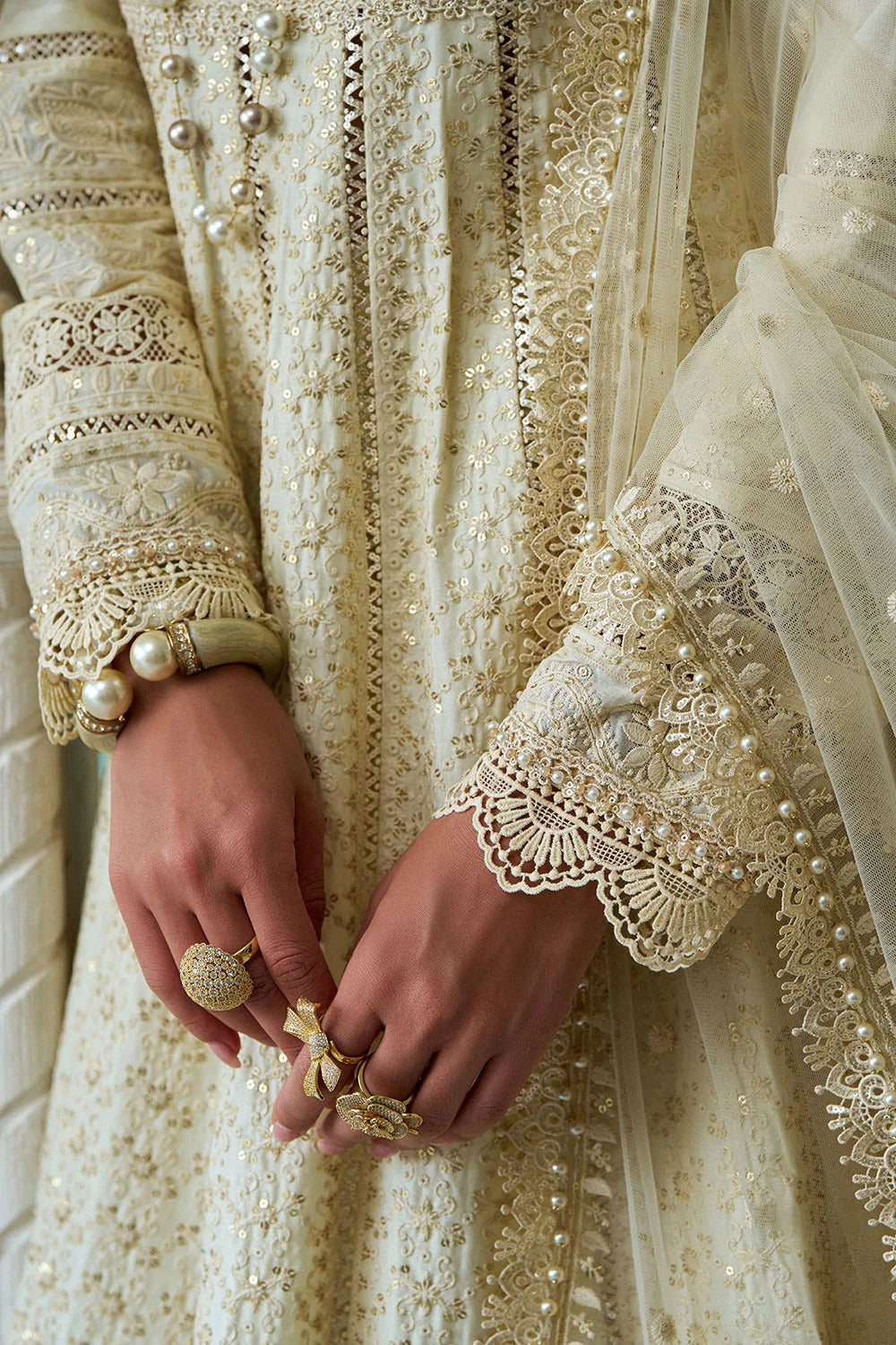 Close-up of hands wearing jewelry with a background of embroidered fabric.