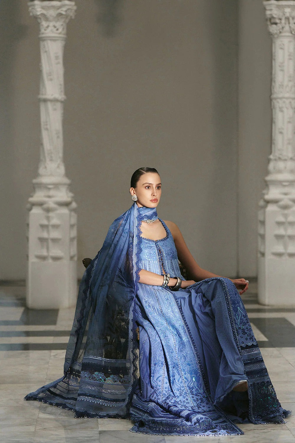 Woman in a blue traditional outfit sitting in an elegant indoor setting.