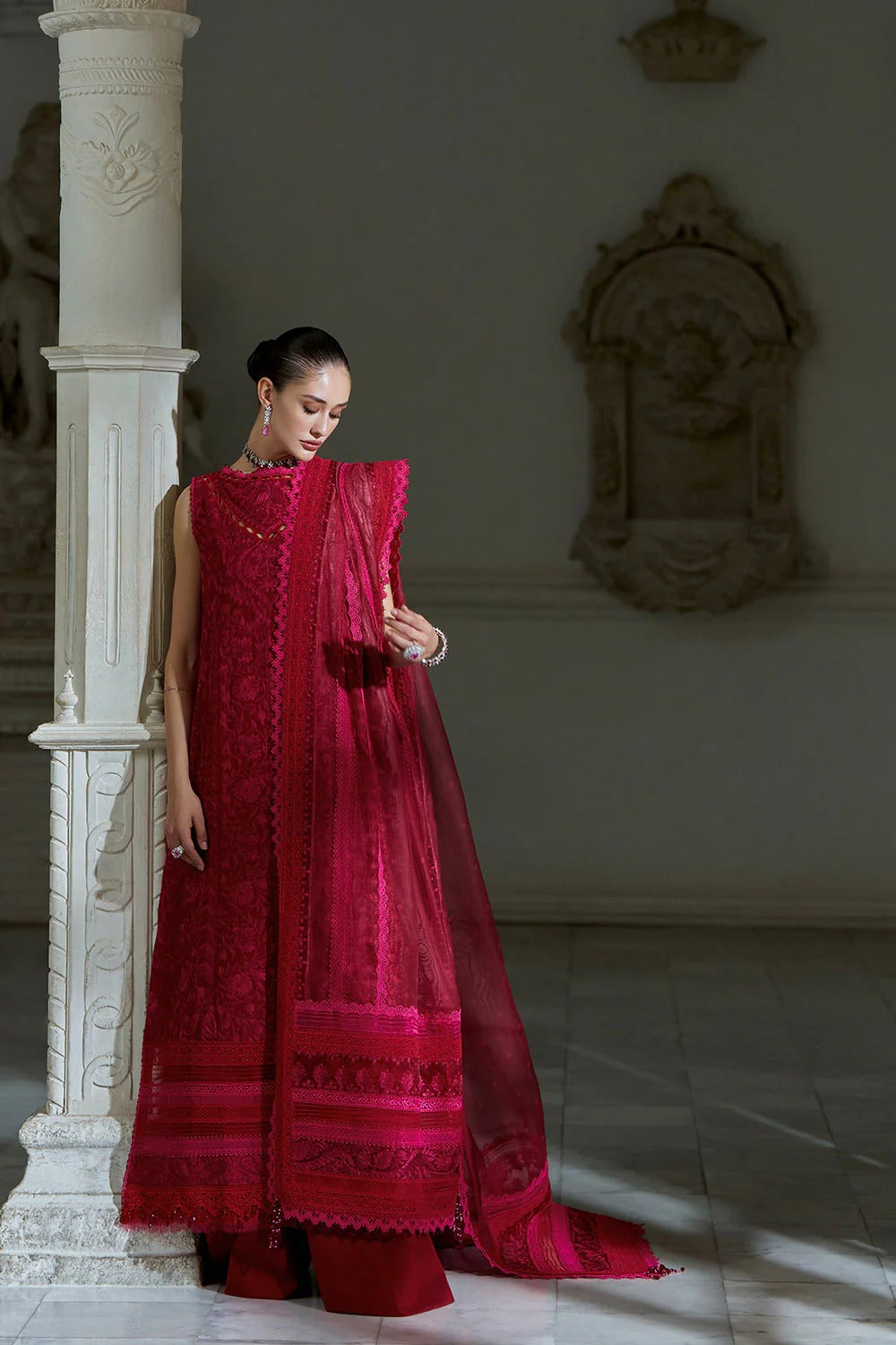Woman in a red traditional outfit standing in a decorative interior setting.