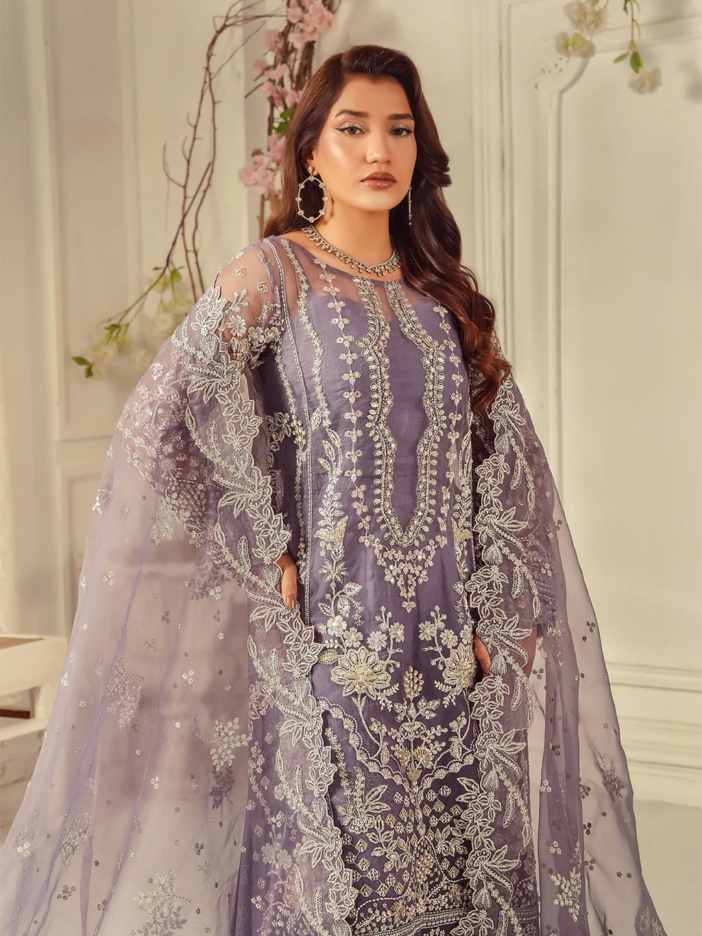Woman wearing a purple embroidered outfit with a sheer overlay in a decorated indoor setting.