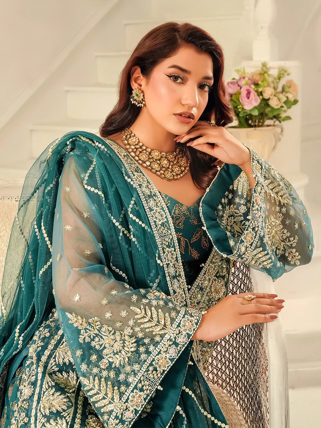 Woman in a teal embroidered traditional outfit with a white background