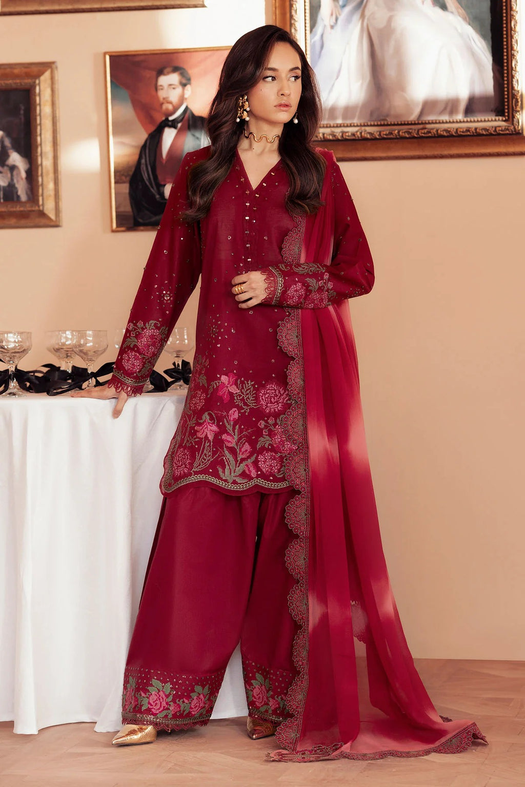 Woman in a red embroidered traditional outfit standing in a room with paintings on the wall.