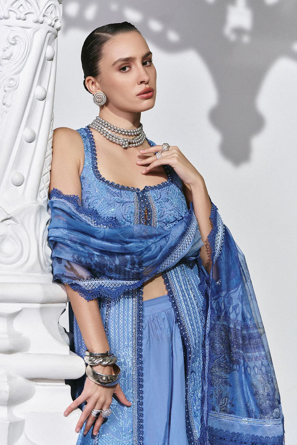 Woman wearing a blue patterned outfit with jewelry against a white background