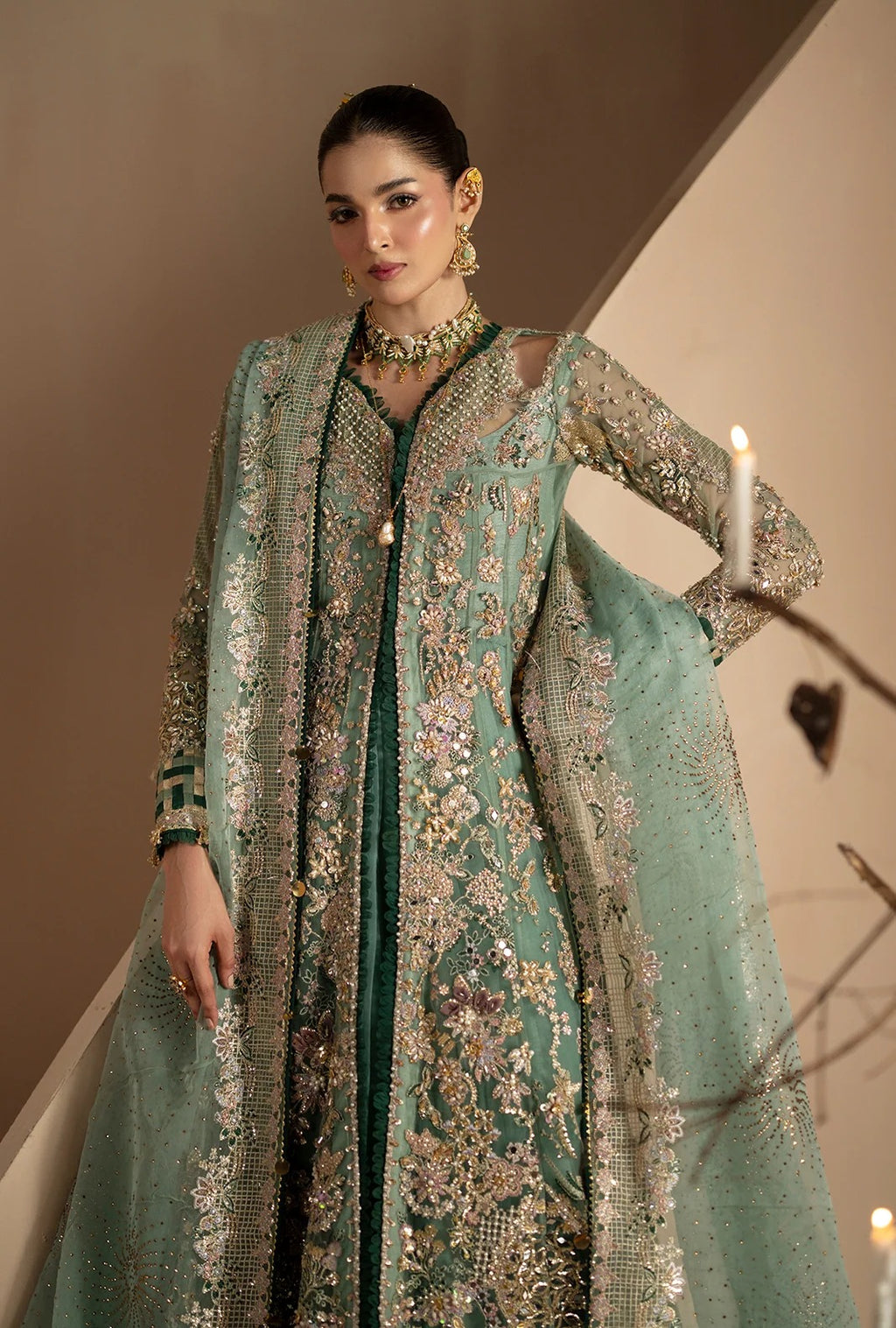 A woman models a traditional South Asian outfit featuring a mint green embroidered kurta with a matching sheer dupatta and a dark green inner layer, decorated with intricate gold and silver embroidery.