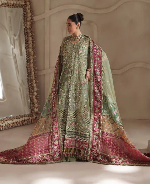 Woman in a traditional embroidered outfit with a pink and green dupatta in a decorated room.