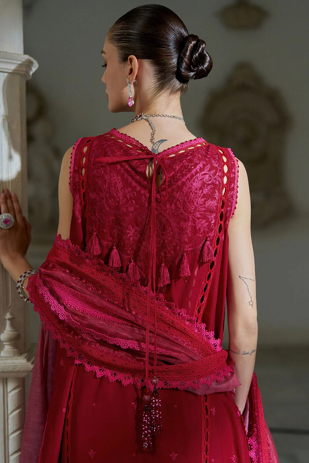 Woman wearing a red lace dress with intricate detailing, standing against a neutral background.