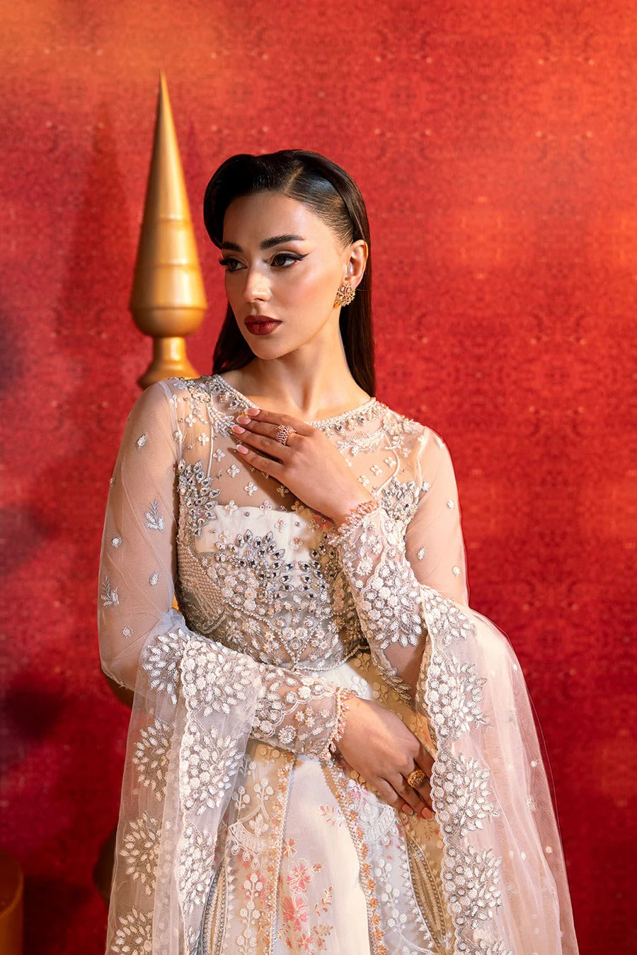 Woman in a white embroidered outfit against a red background