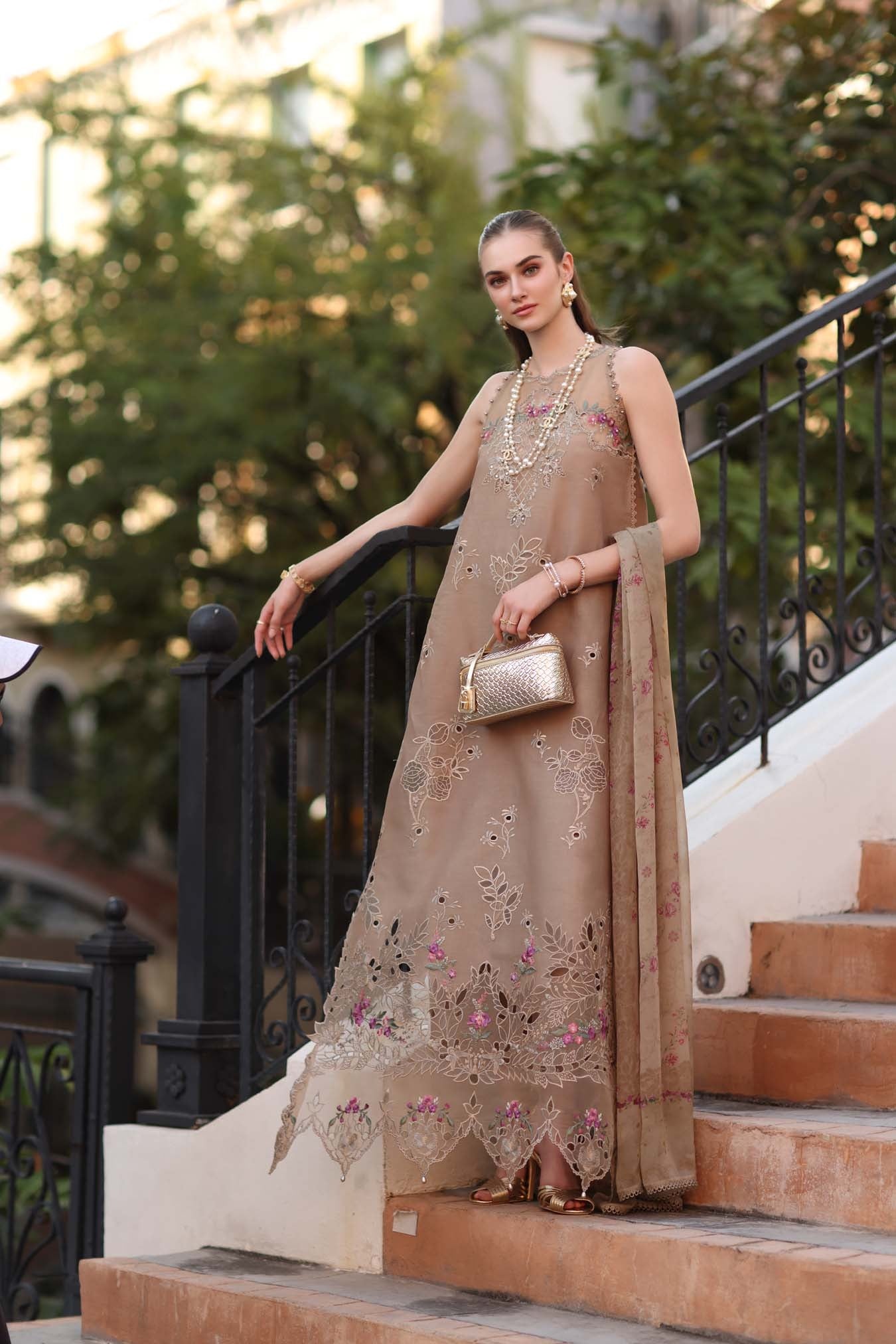 Woman in a beige embroidered dress standing on steps outdoors